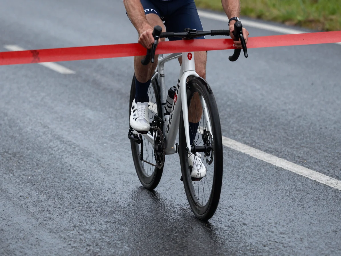 Close action detail of a rider crossing a finish line on wet asphalt, deep charcoal palette with a red race number, over